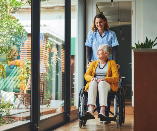 Shot of a young nurse pushing a senior woman in a wheelchair in a retirement home